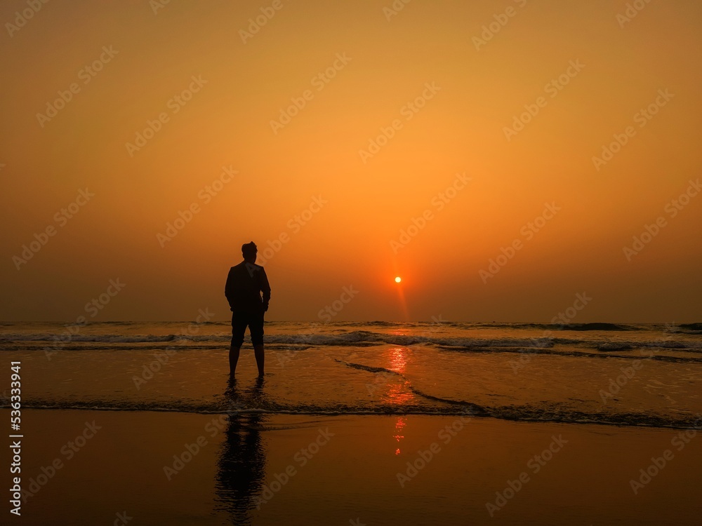The silhouette of a young man admires the sunset on the sea. healthy lifestyle. freedom, inspiration, Nature, and beauty concept. Orange sundown.