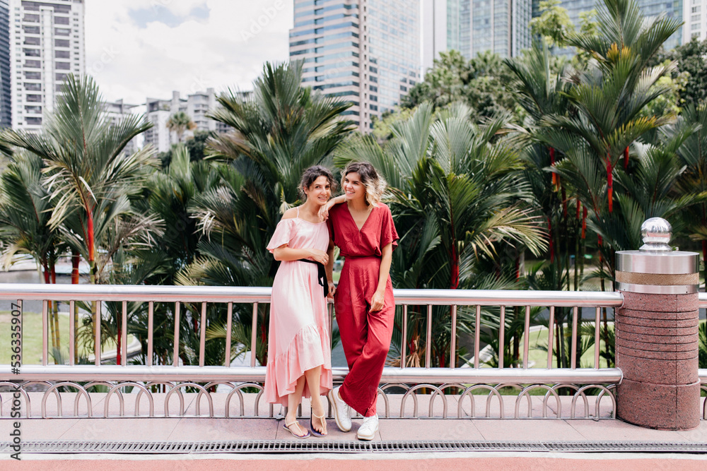 Full-length photo of romantic european lady in dress spending vacation with sister. Outdoor portrait of adorable girls having fun during summer travel. Full-length photo of romantic european lady in dress spending vacation with sister. Outdoor portrait of adorable girls having fun during summer travel.