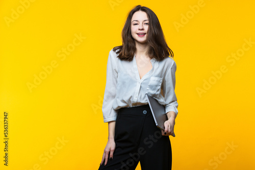 Portrait of a young woman with a laptop in her hands on a yellow background. © makedonski2015
