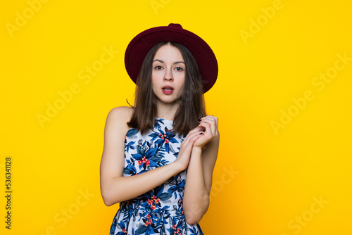 A young woman in a dress and hat on a yellow background.