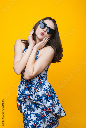 Brunette in a dress and sunglasses on a yellow background.