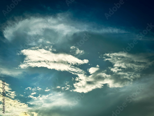 Natural sky and clouds background. Cloud cover over trees and mountains, evening soft sunlight.