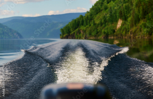 The boat cuts the surface of the lake water of Lake Teletskoye, Altai Republic, Russia.