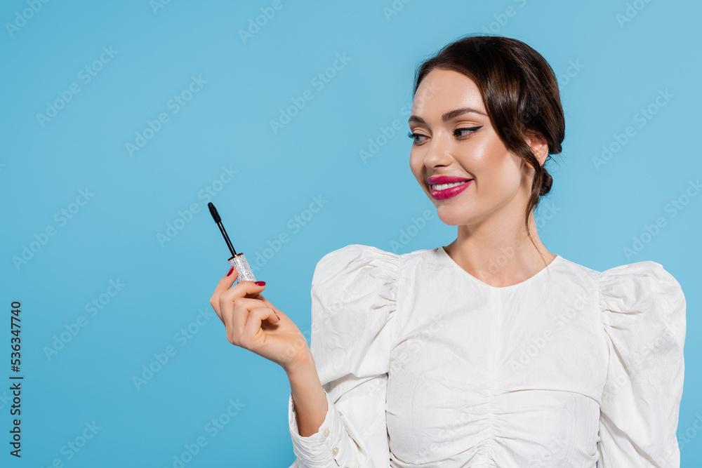 cheerful young woman in white blouse holding mascara brush isolated on blue. cheerful young woman in white blouse holding mascara brush isolated on blue.