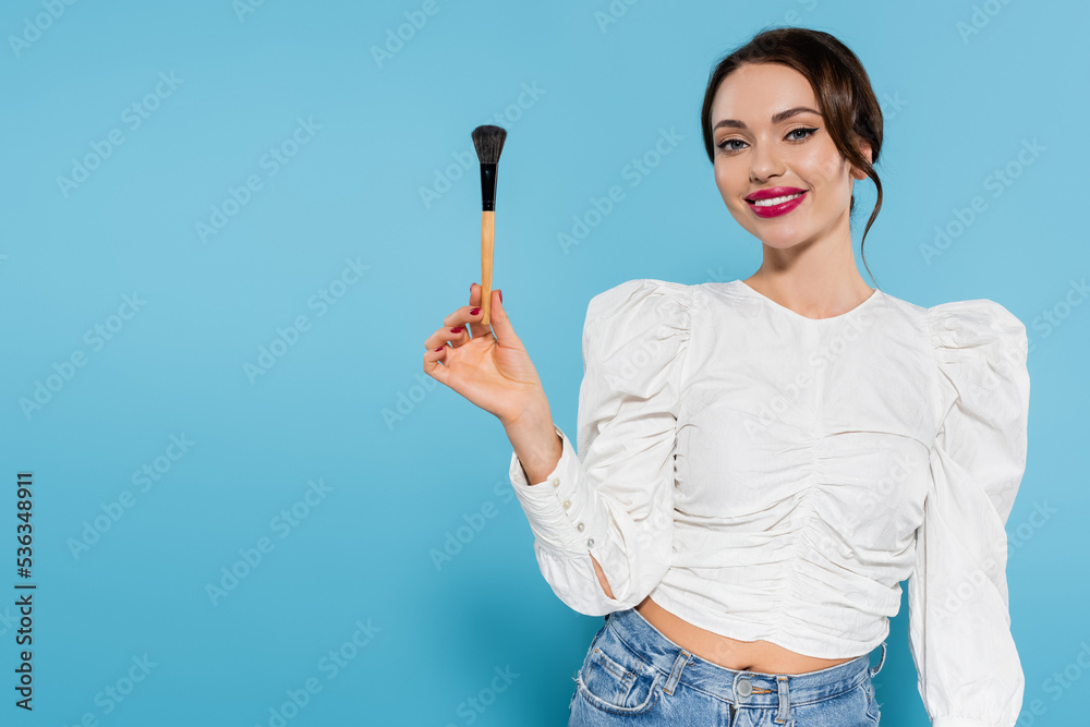 cheerful young woman in white blouse holding cosmetic brush and smiling on blue. cheerful young woman in white blouse holding cosmetic brush and smiling on blue.