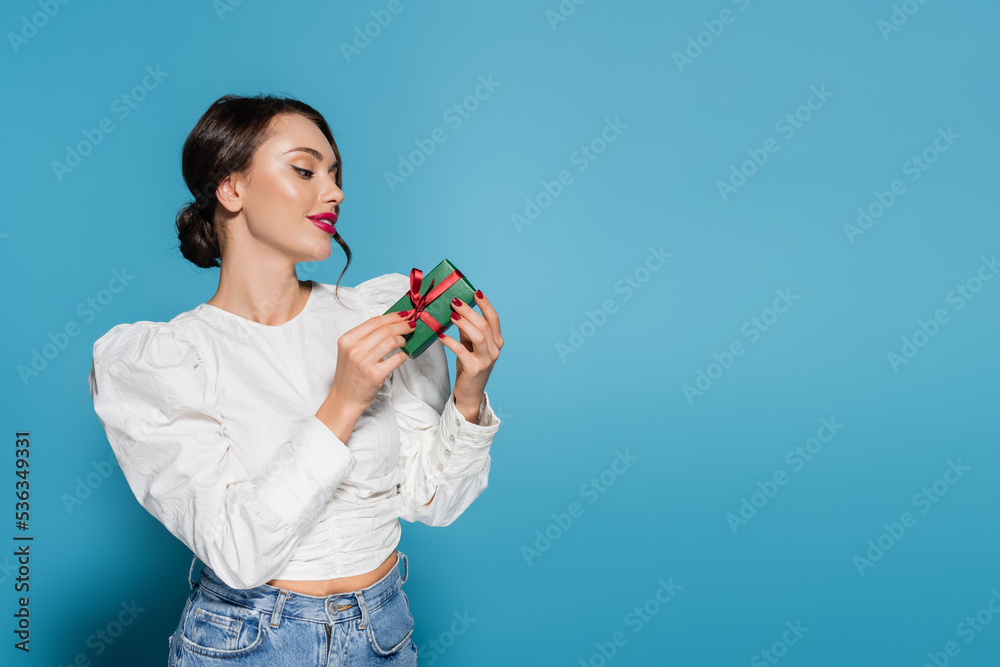 happy young woman in white blouse looking at wrapped present on blue. happy young woman in white blouse looking at wrapped present on blue.