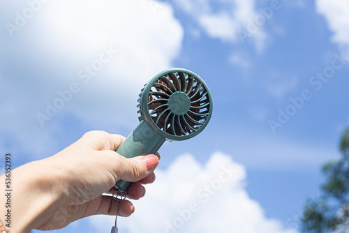 Mini portable blue electric fan. Hand holding bunny look like electric fan in blue cloudy background.