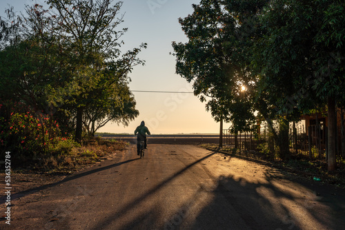 Fototapeta Naklejka Na Ścianę i Meble -  Worker cyclist heading towards the highway at illuminated sunrise