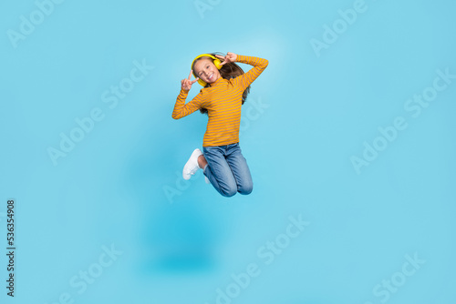 Full body portrait of excited carefree girl jumping demonstrate v-sign isolated on blue color background