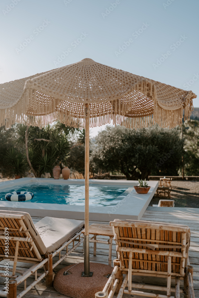 Fototapeta premium The relaxing scene of a swimming pool area, sun umbrella, trees and loungers at sunset in Rhodes Island, Greece