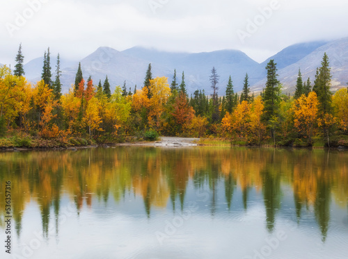 Equilibrium on an autumn lake in the northern mountains with a colorful and multi colored forest in rain