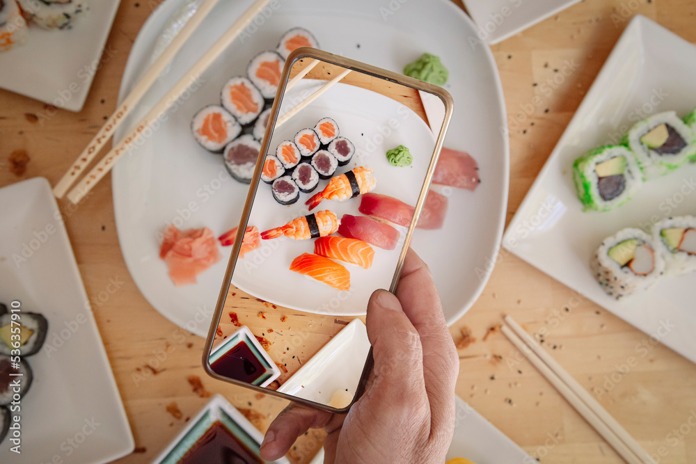 Man with mobile phone taking photo of delicious sushi on table, top view