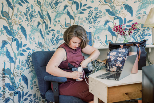 Short-haired Caucasian mother inserts breast pump at desk. photo