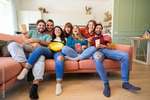 Group of roommates watching tv and eating snack sitting on the couch - Cheerful young students having fun in living room