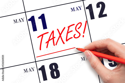 Hand drawing red line and writing the text Taxes on calendar date May 11. Remind date of tax payment
