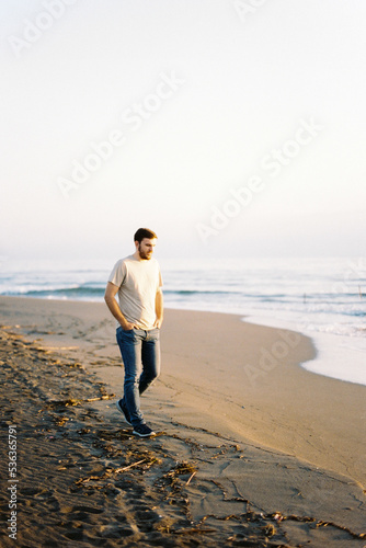 Young man in jeans walking along the sandy beach near the water