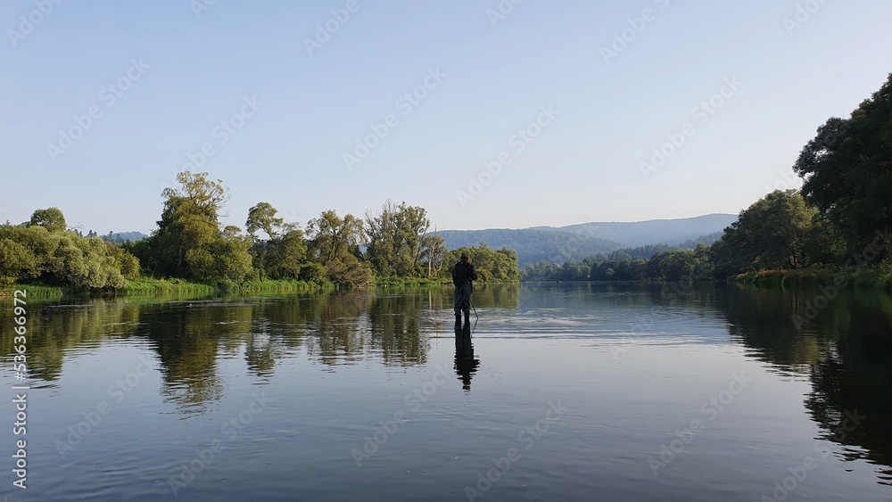 Silhouette of a fisherman, a rod and a breathtaking scene in the forest with colourful reflections on the river. Article about fishing day hunting for a trout. Silhouette of a fisherman, a rod and a breathtaking scene in the forest with colourful reflections on the river. Article about fishing day hunting for a trout.