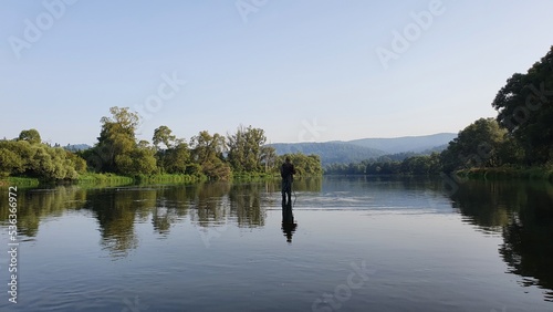 Silhouette of a fisherman, a rod and a breathtaking scene in the forest with colourful reflections on the river. Article about fishing day hunting for a trout.