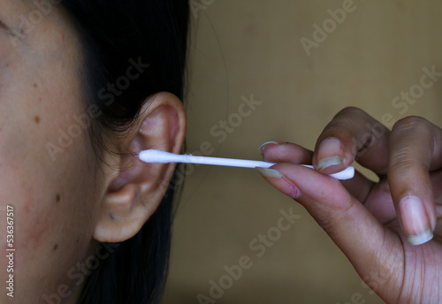 Woman uses ear cleaning cotton bud to clear her ear.