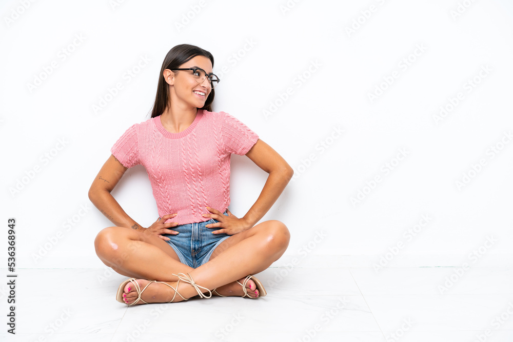 Young caucasian woman sitting on the floor isolated on white background posing with arms at hip and smiling Young caucasian woman sitting on the floor isolated on white background posing with arms at hip and smiling