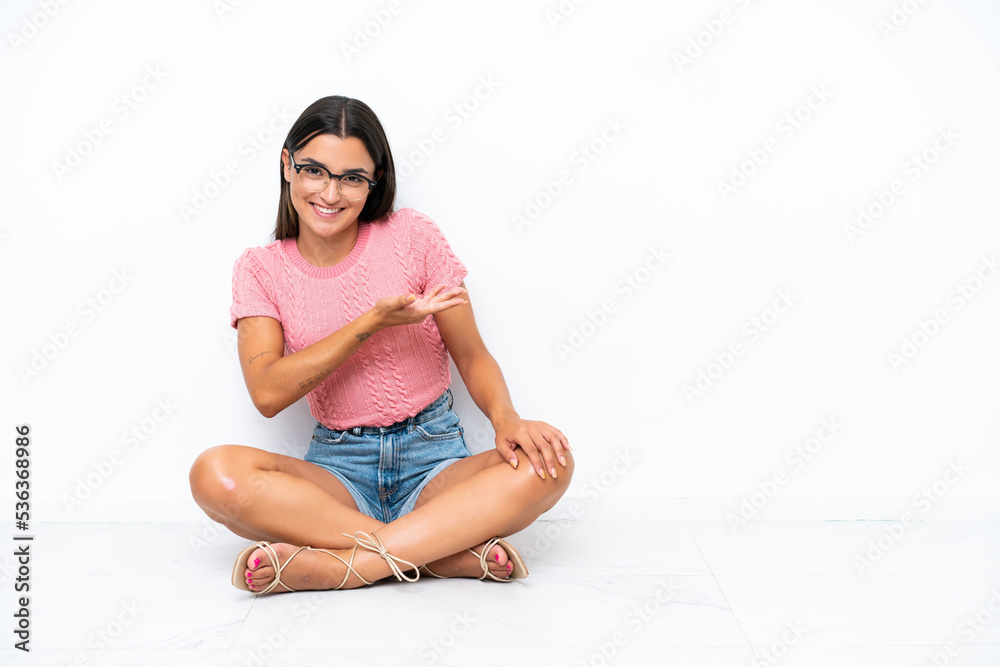 Young caucasian woman sitting on the floor isolated on white background presenting an idea while looking smiling towards Young caucasian woman sitting on the floor isolated on white background presenting an idea while looking smiling towards