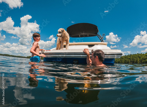 Man and child swimming off the back of a boat on a summer day.