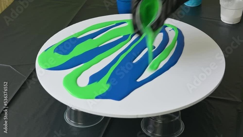 epoxy resin with blue and green hues is poured onto canvas to create a painting