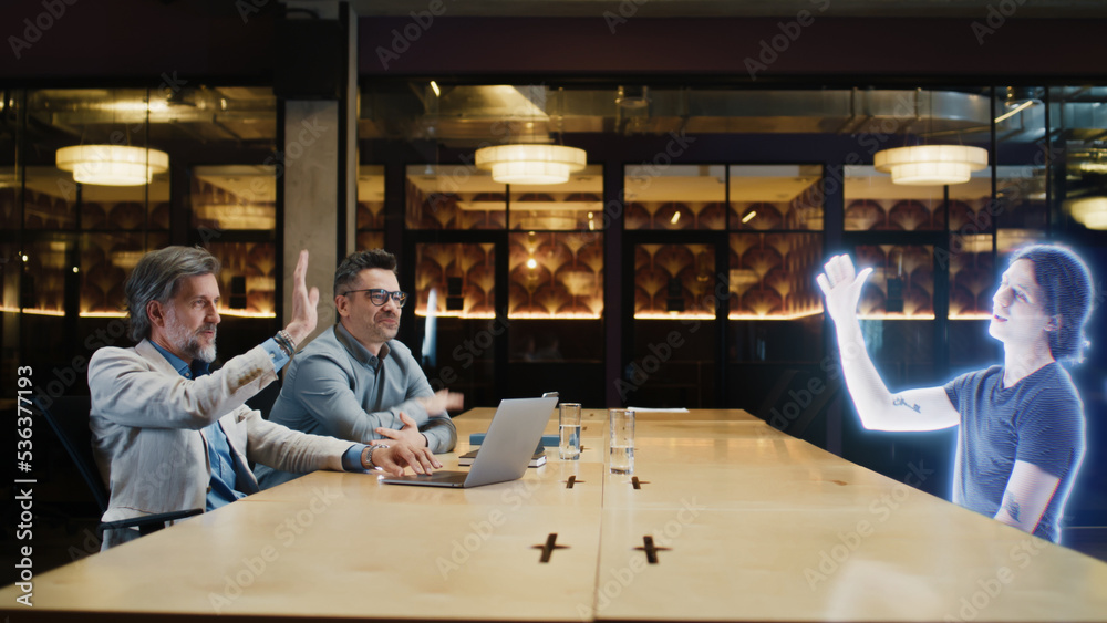 The concept of futuristic business collaborations and negotiations. Two adult businessmen in casual clothes connect and have an online meeting with a young employee using a metaverse holographic link The concept of futuristic business collaborations and negotiations. Two adult businessmen in casual clothes connect and have an online meeting with a young employee using a metaverse holographic link