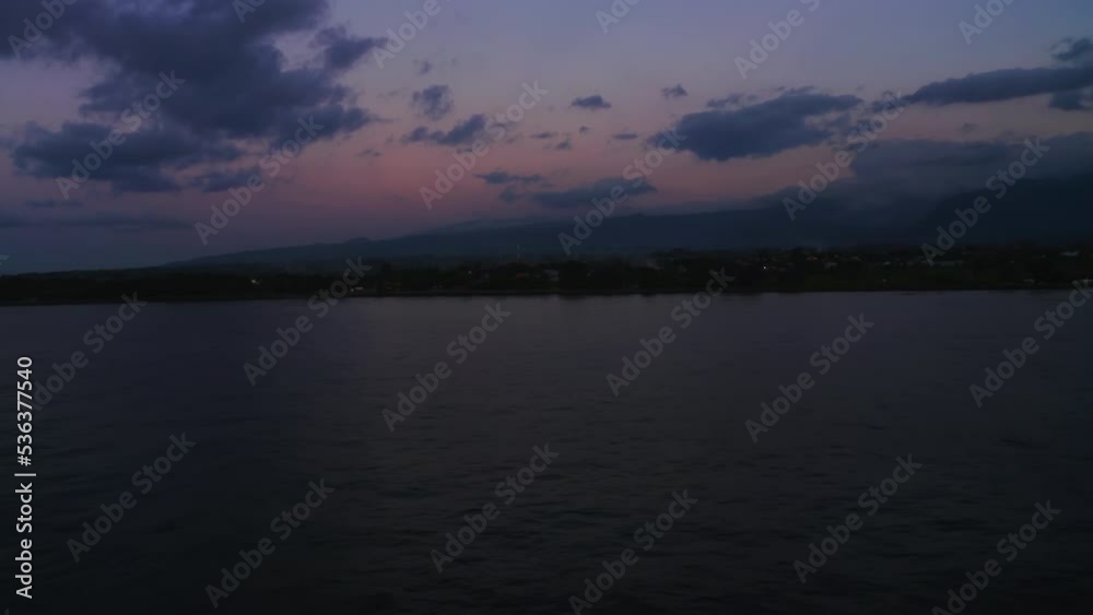 Night scenery on a full moon, the drone flies over the surface of the ocean and lifts the camera up and offers a panoramic view of the coast with dark mountains and the sunset sky. Aerial footage Night scenery on a full moon, the drone flies over the surface of the ocean and lifts the camera up and offers a panoramic view of the coast with dark mountains and the sunset sky. Aerial footage
