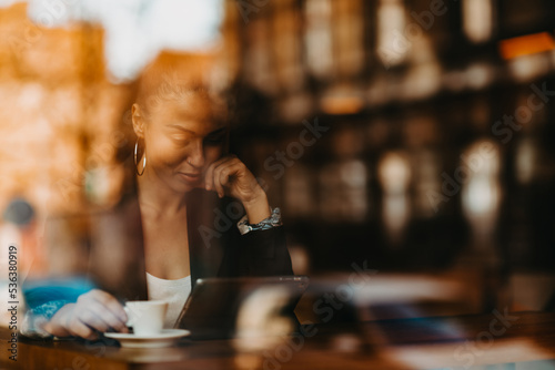 woman in a coffee shop drink coffee viewed through glass with reflections as they sit at a table chatting and laughing