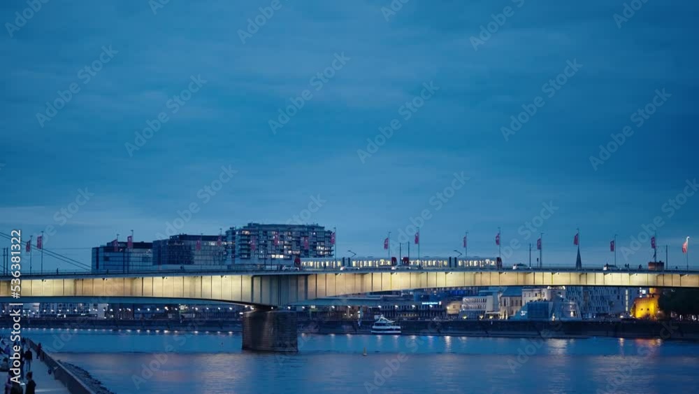 Train and car vehicles traffic on illuninated Deutz bridge in Cologne at the evening with view of the famous Kranhaus building complex with crane house on riverside of Rhein at background, slow motion Train and car vehicles traffic on illuninated Deutz bridge in Cologne at the evening with view of the famous Kranhaus building complex with crane house on riverside of Rhein at background, slow motion