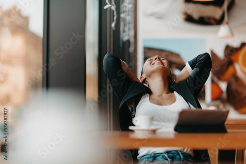 A woman sits in a cafe with her arms raised and celebrating a job well done.Business concept