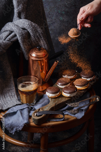Female hand pouring with cocoa powder homemade delicious cookies. Coffee, cakes and cozy sweater in dark style as autumn season concept. Copy space