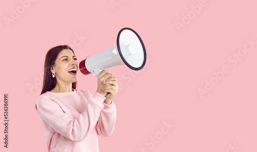 Smiling young Caucasian woman isolated on pink studio background make announcement in megaphone. Millennial girl get attention talk in loudspeaker about good promotion or seasonal sale.