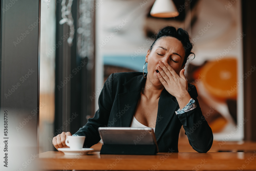 A sleepy woman sits in a cafe during a break and uses a tablet.Business concept. A sleepy woman sits in a cafe during a break and uses a tablet.Business concept.