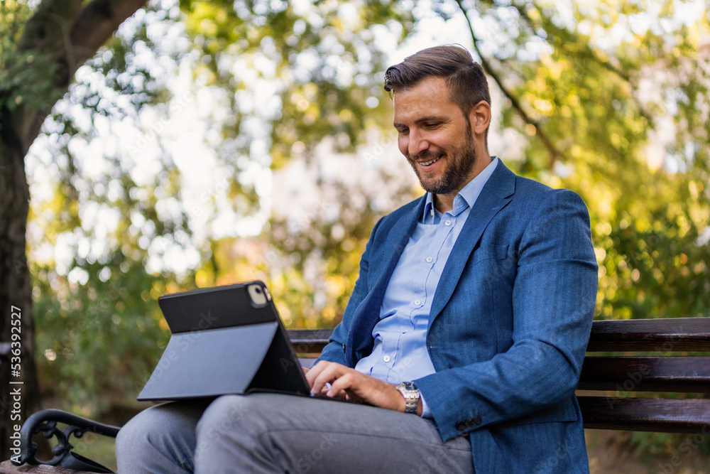 Portrait of happy entrepreneur working on laptop\tablet while sitting on park bench. Portrait of happy entrepreneur working on laptop\tablet while sitting on park bench.