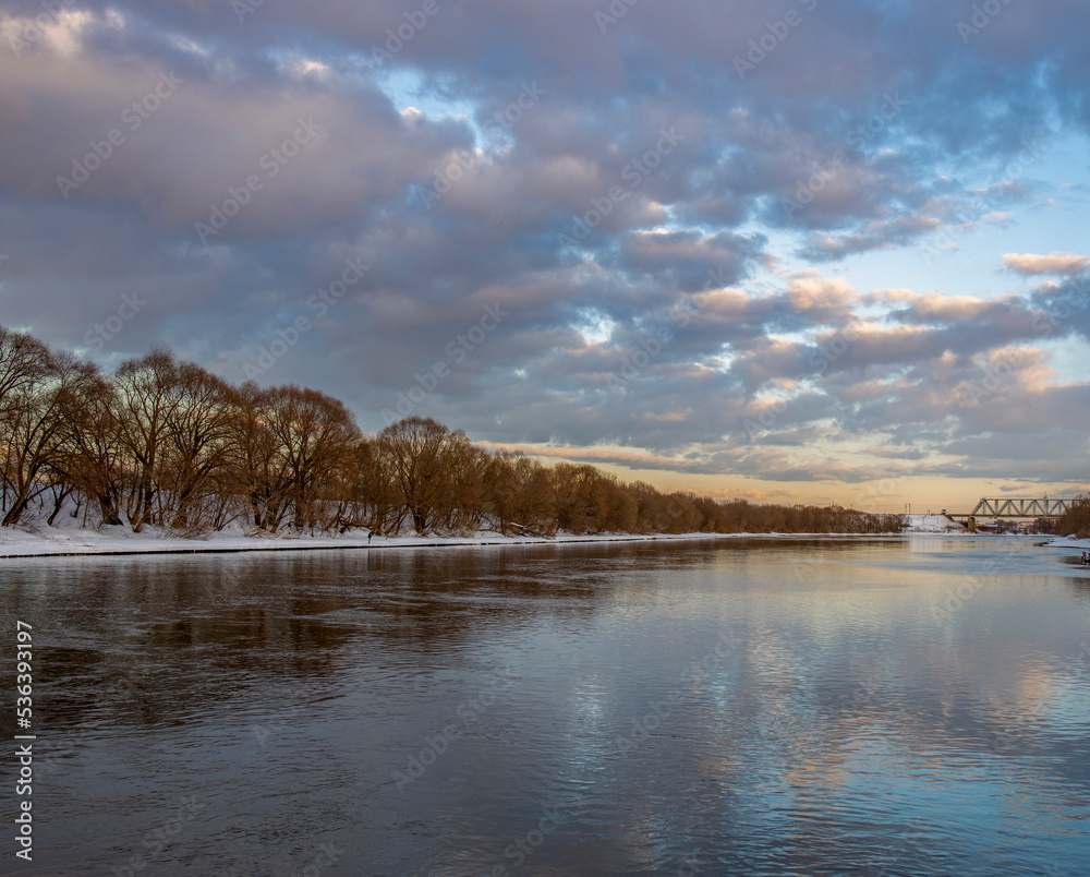 Winter evening landscape with clouds, river and trees.