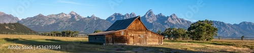 Panoramic shot of a wooden house in a field in Mormon Row, Utah and Yellowstone National Park