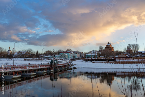 Fototapeta Naklejka Na Ścianę i Meble -  Clouds over the old city. Winter evening. pedestrian pontoon bridge across the river.