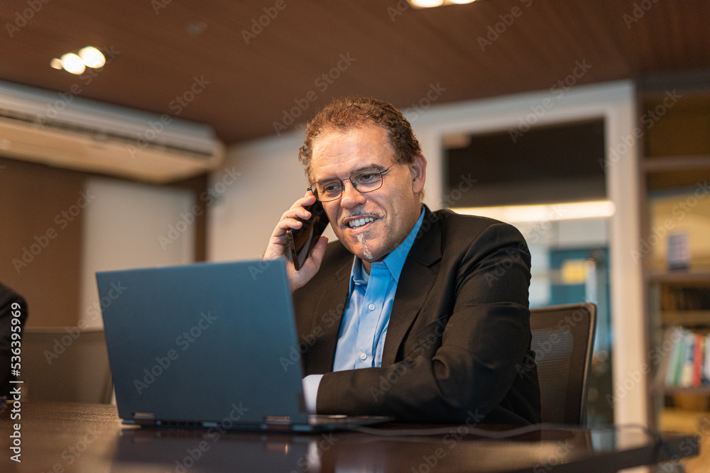Portrait of mature businessman using laptop computer and mobile phone in office horizontal shot