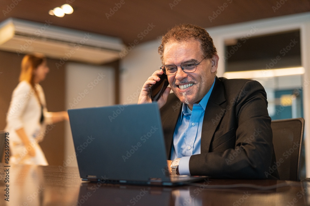 Portrait of mature businessman using laptop computer and mobile phone in office horizontal shot Portrait of mature businessman using laptop computer and mobile phone in office horizontal shot