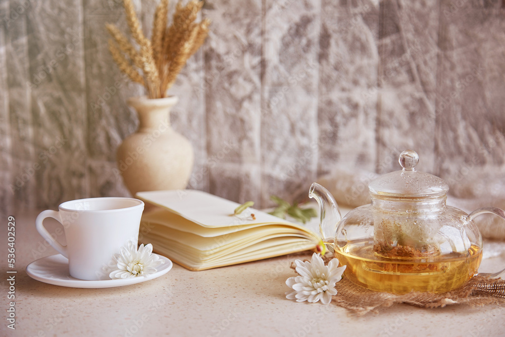 Fototapeta premium Herbal linden tea in teapot with cup of tea. Wheat,flowers, autumn decorations and notebook. Cozy atmosphere relax at home.