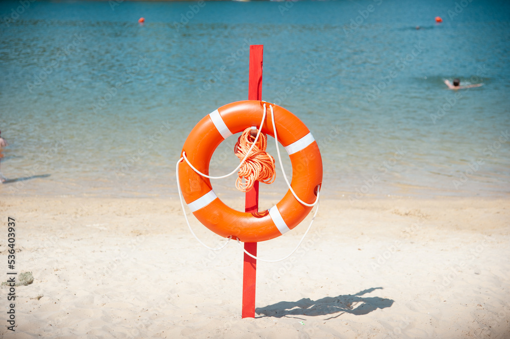 Orange life buoy on the sea or ocean. Sunny sandy beach.