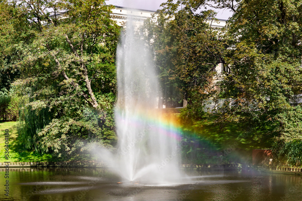 Panorama of the beautiful Riga canal and fountain with a rainbow near Bastion park, Riga center, capital of Latvia. Rainbow from city fountain splash water drops