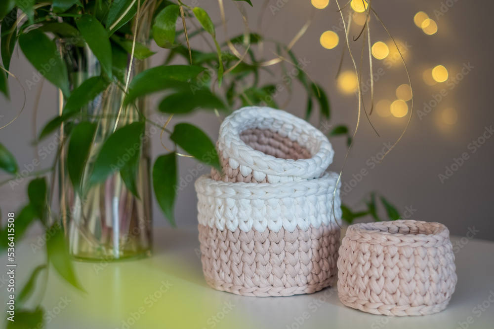 Beige cute decorative hand crocheted baskets, sustainable handicraft business, cozy Christmas atmosphere with decorative plants and blurred Christmas lights in the background