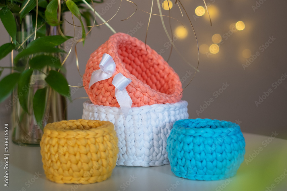 Colorful cute decorative hand crocheted baskets, sustainable handicraft business, cozy Christmas atmosphere with decorative plants and blurred Christmas lights in the background