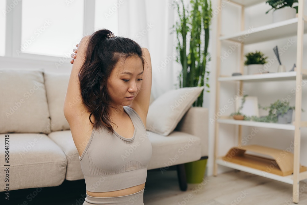 Young Asian woman her laptop doing sports and yoga repeating exercises on the video at home in the lotus position stretching the muscles of the back and arms, home workouts for the body lifestyle Young Asian woman her laptop doing sports and yoga repeating exercises on the video at home in the lotus position stretching the muscles of the back and arms, home workouts for the body lifestyle
