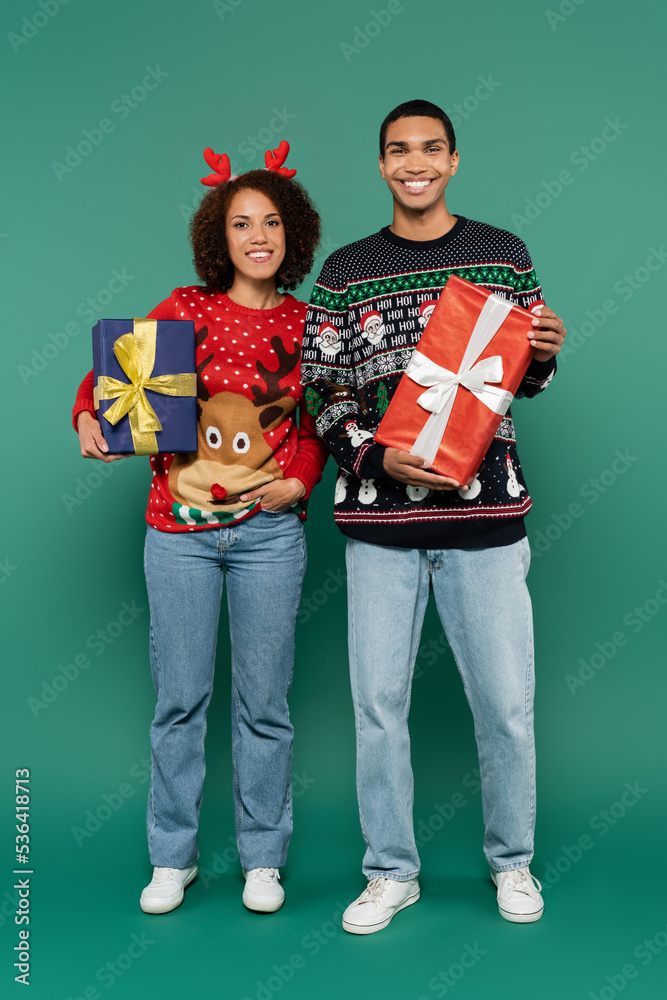 full length of african american couple in festive outfit holding christmas presents and smiling at camera on green background full length of african american couple in festive outfit holding christmas presents and smiling at camera on green background