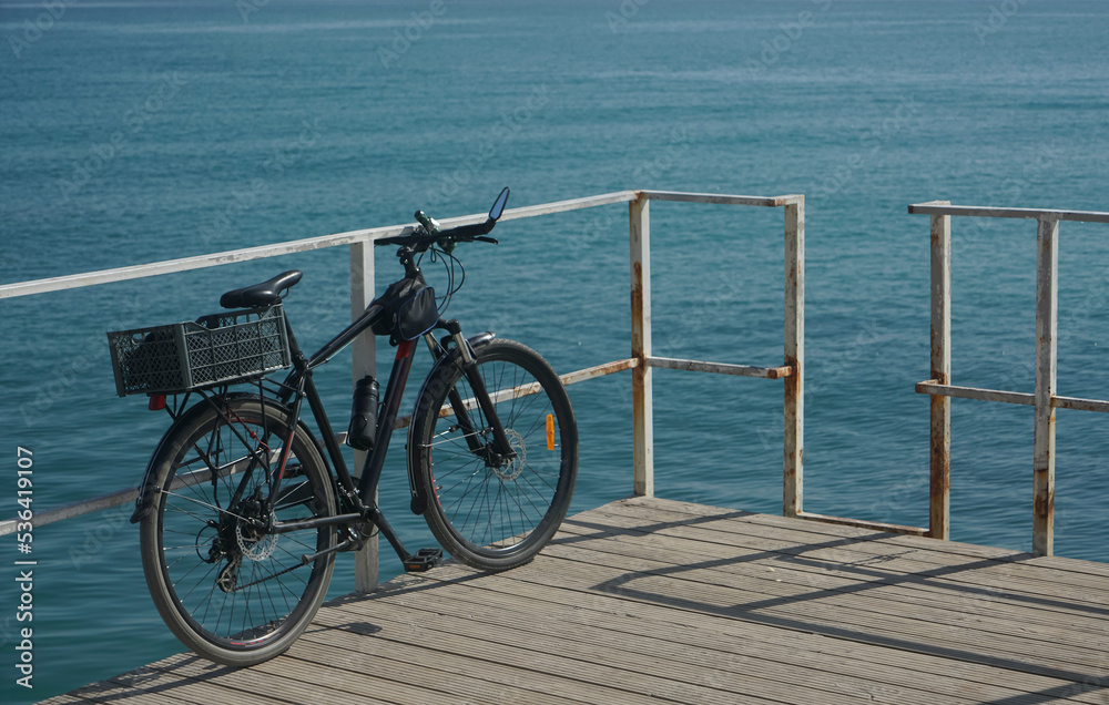 Fototapeta premium End of a bike trip. black modern bicycle with plastic box and bottle of water on a wooden pier over Caspian Sea water. Aktau, kazakhstan