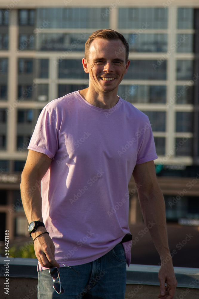 A handsome guy in denim shorts and a pink t-shirt poses beautifully in the city A handsome guy in denim shorts and a pink t-shirt poses beautifully in the city